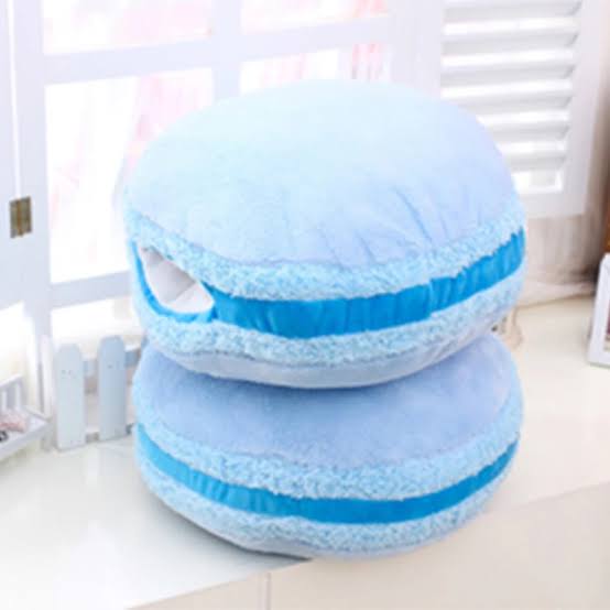 Pastel macaron shaped plushies in pink, mint, and lavender stacked on a bed